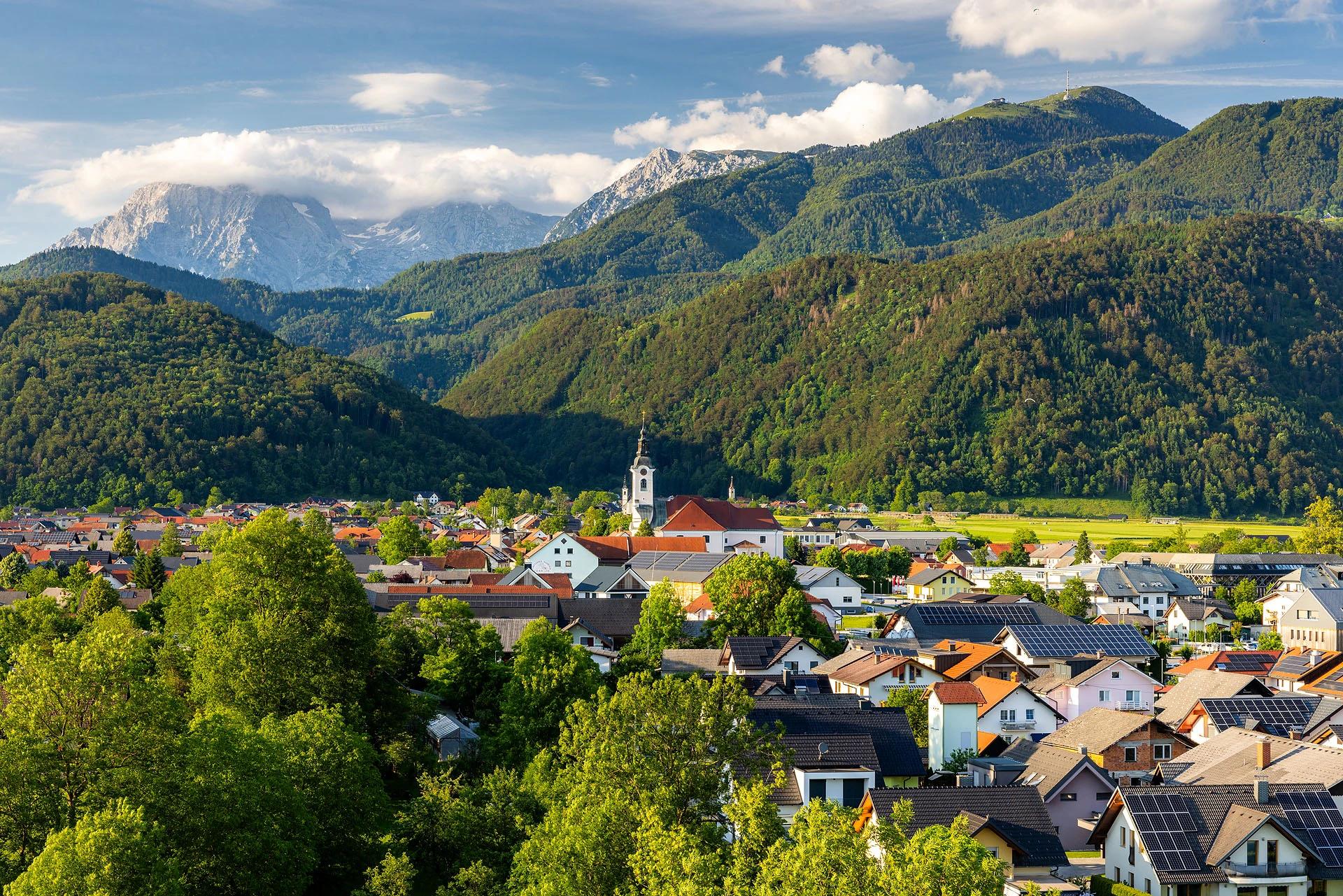 Cerklje z župnijsko cerkvijo pod gozdnatimi pobočji Krvavca in vrhovi Kamniško-Savinjskih Alp.